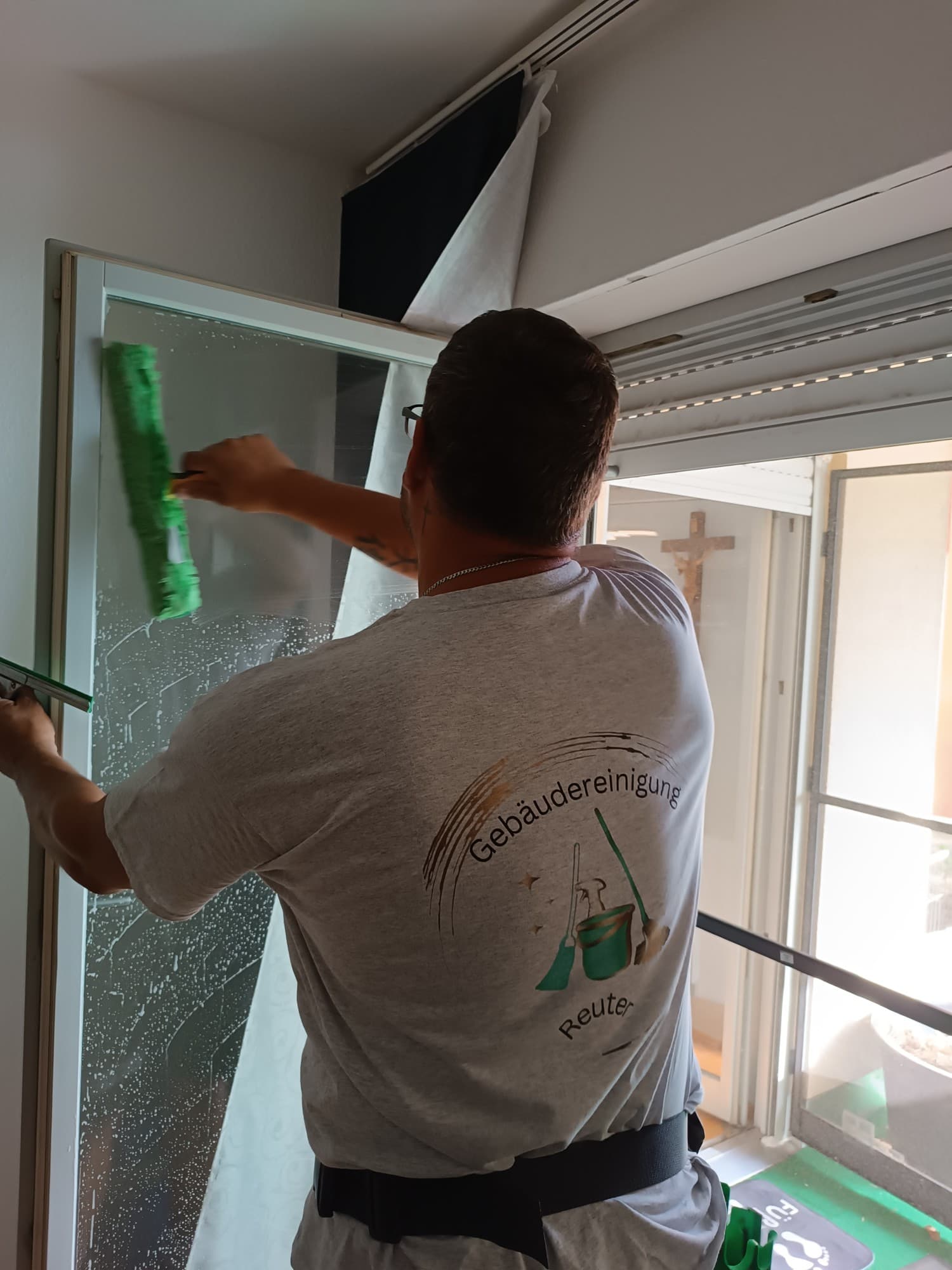 Person vom Team Gebäudereinigung Reuter von hinten beim Fensterputzen mit Einwascher, Firmenlogo auf dem Shirt